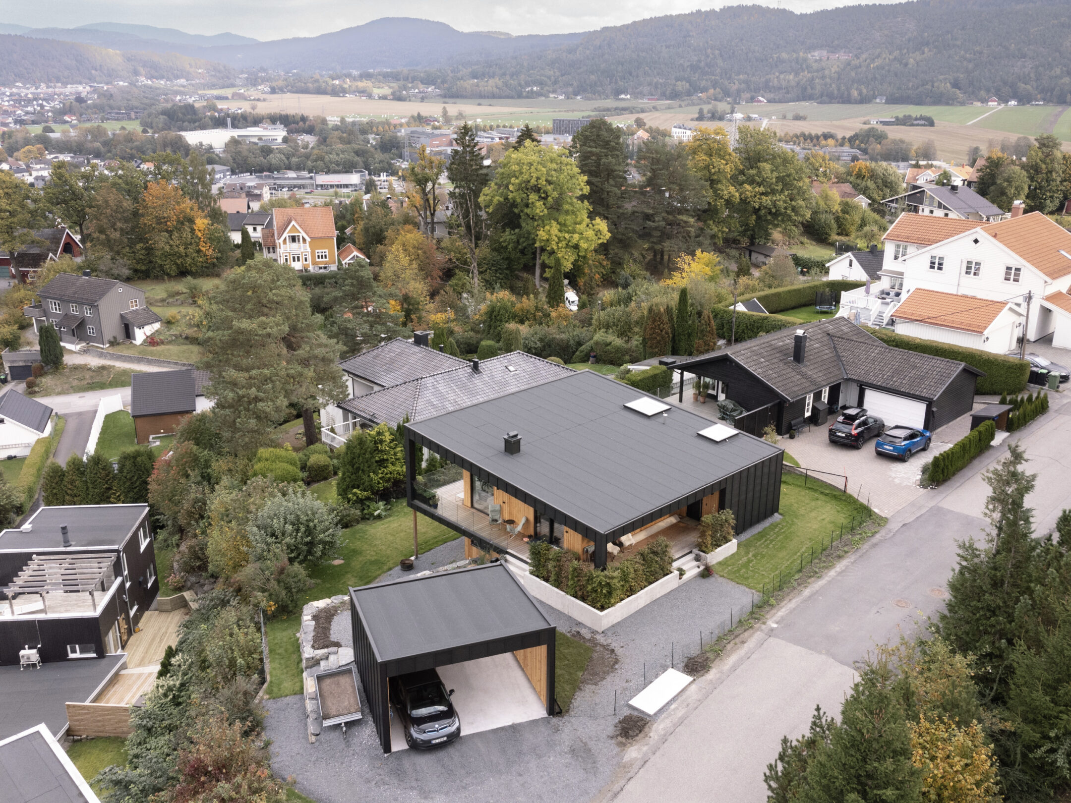 Aerial view of a hilly suburban neighborhood with modern black-roofed houses, driveways, and green yards.