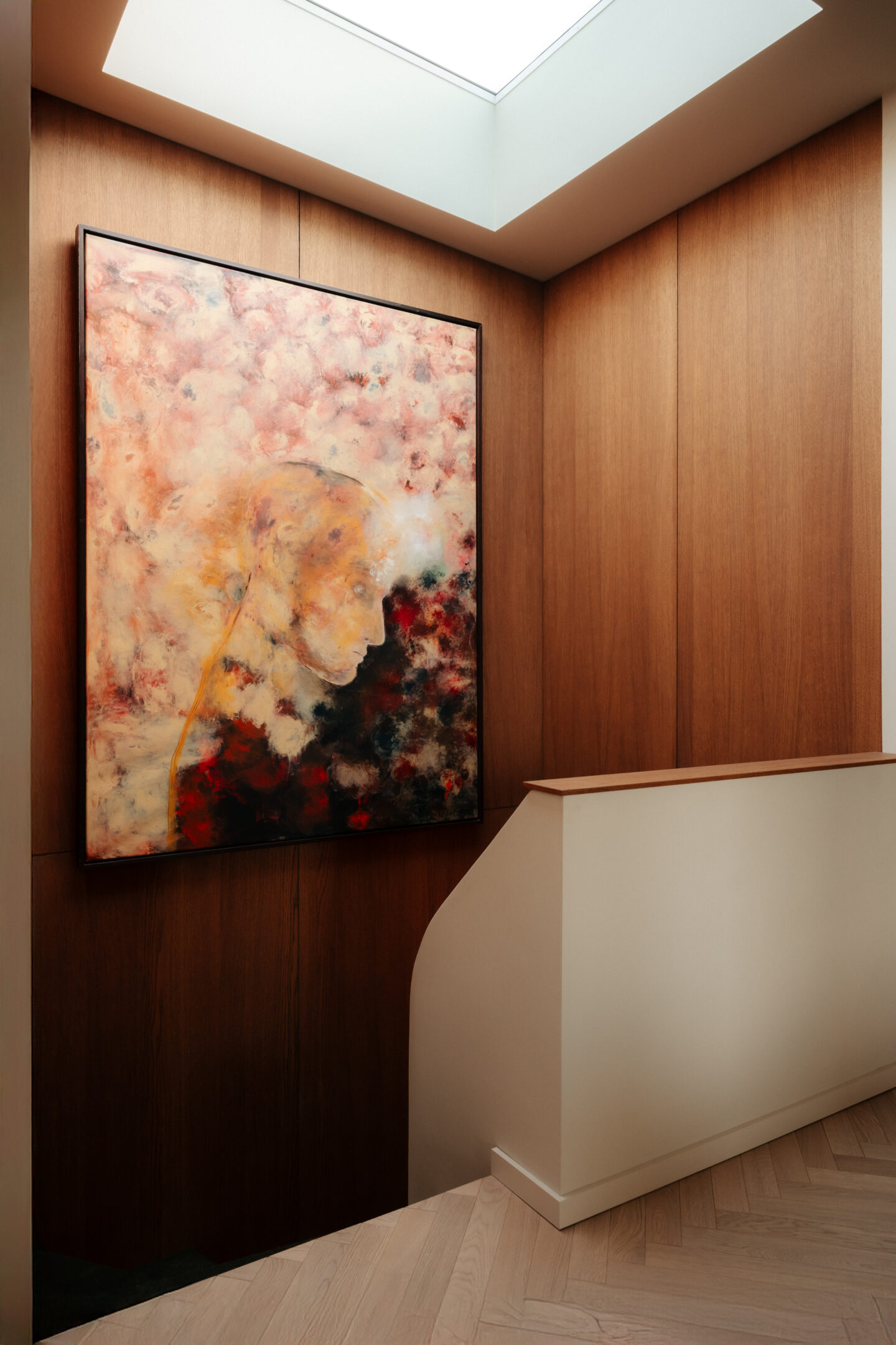 Interior corner with wood-paneled walls, a large abstract painting, a skylight above, and a white curved railing.